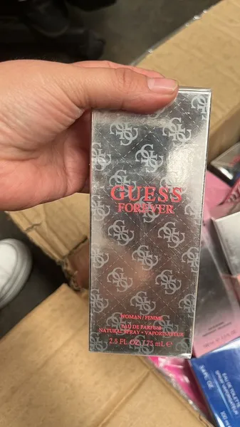 Vista de perfume junto a una caja llena de perfumes de marca listo para la compra de mayoreo cerca de ti